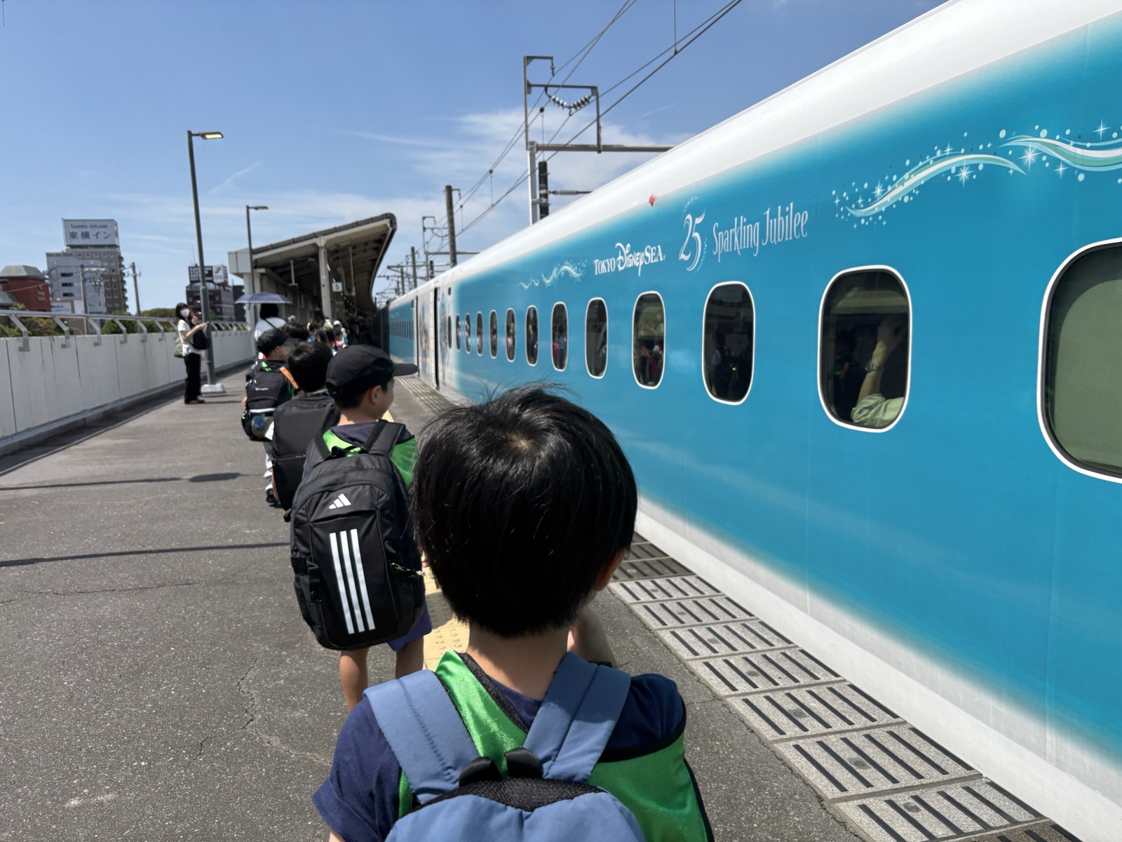 ホームに停まる新幹線と、リュックを背負って並ぶ子どもたちの後ろ姿