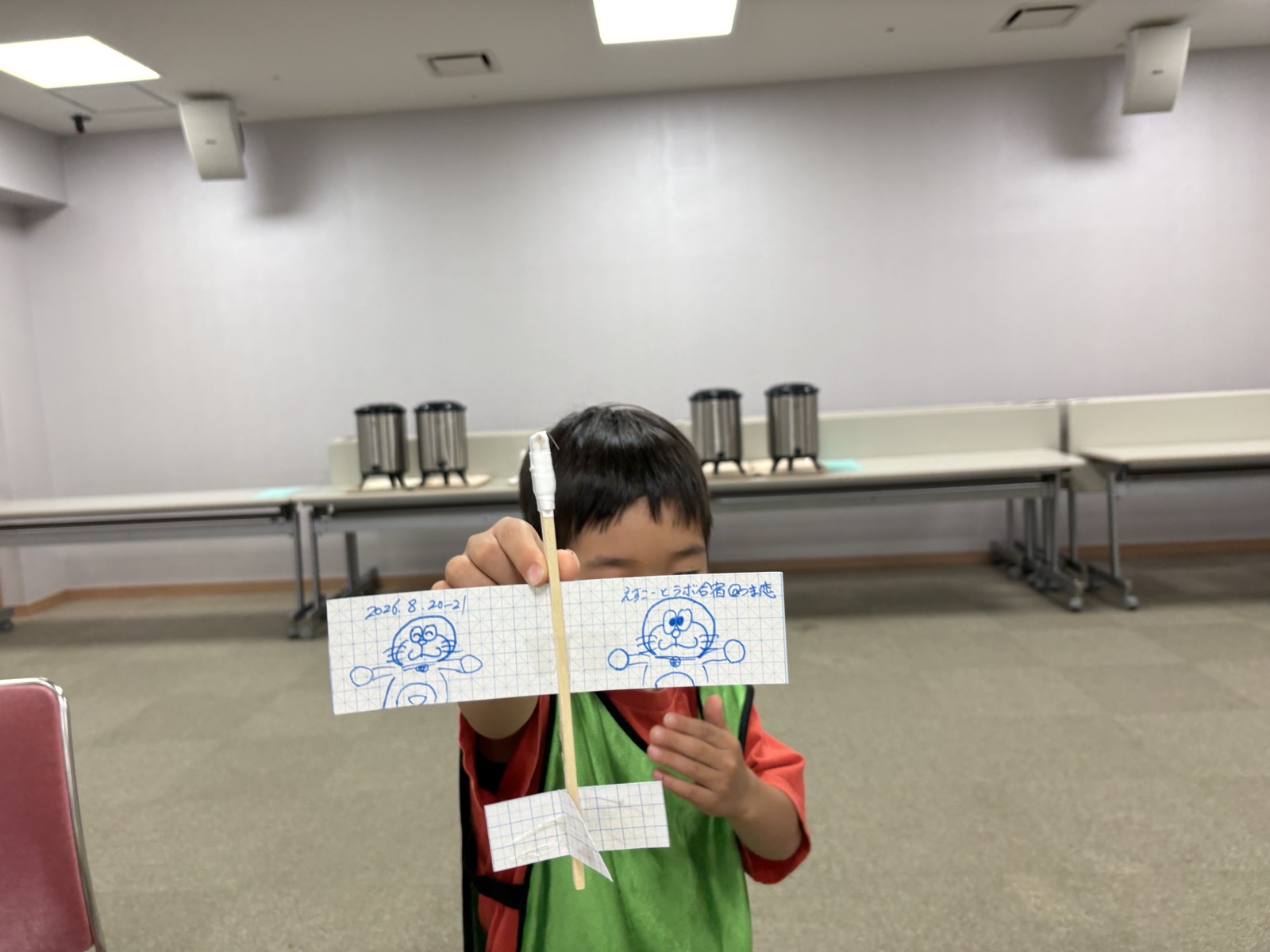 割り箸と方眼紙で作った模型飛行機を掲げる子ども
