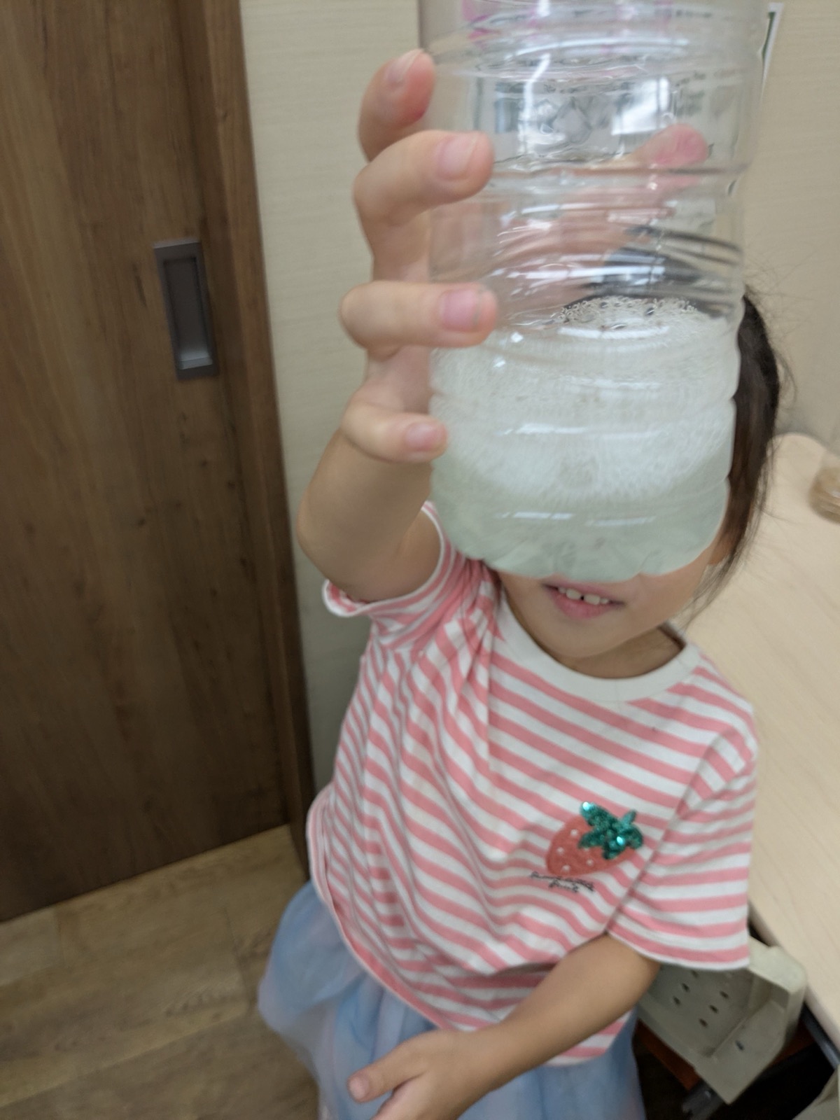 液の入ったペットボトルを顔の前に掲げる子ども