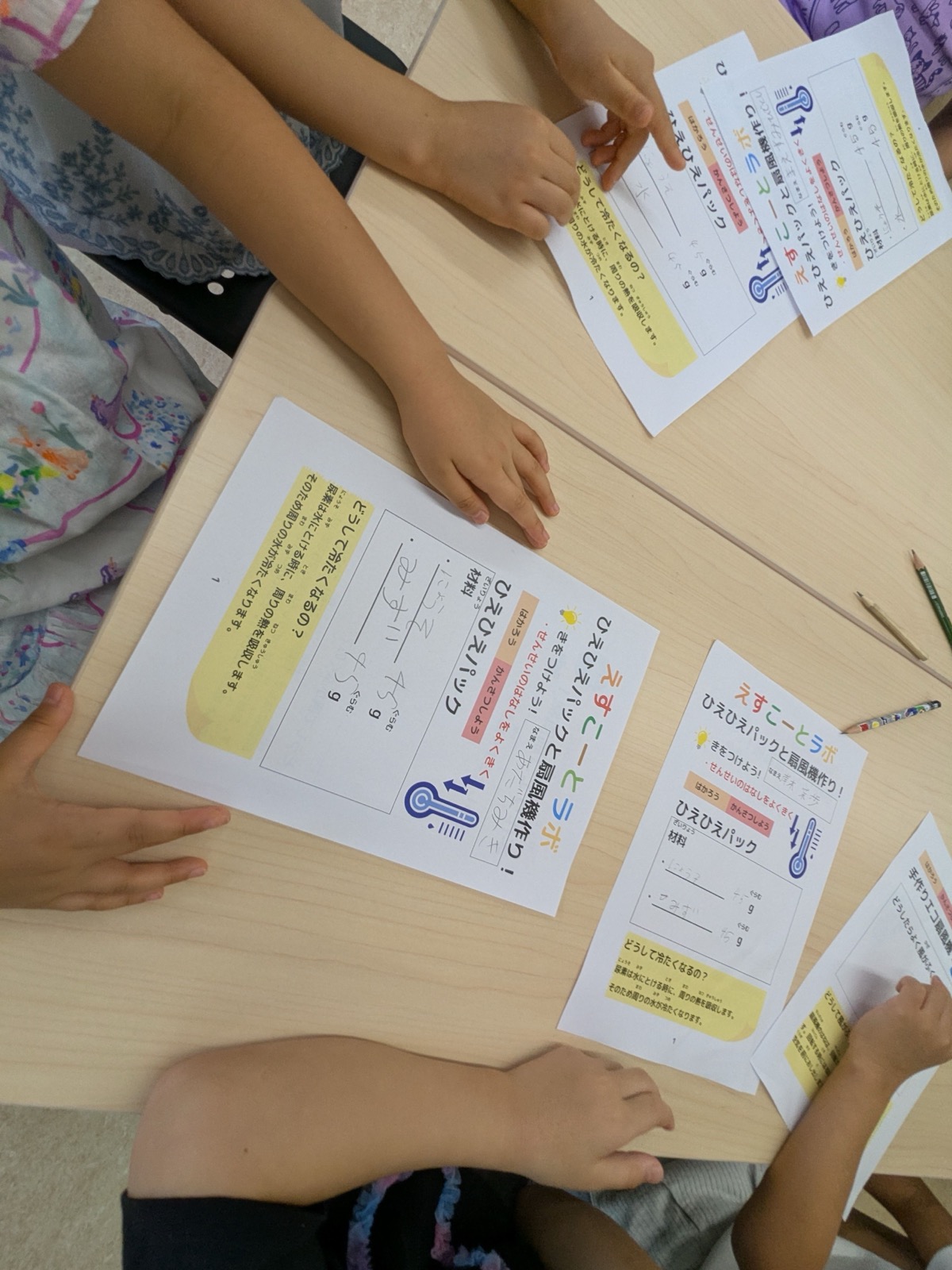 冷却パックと扇風機作りの手順プリントを囲む子どもたちの手